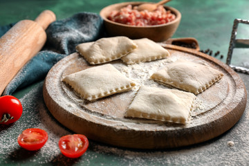 Wooden board with raw ravioli on table