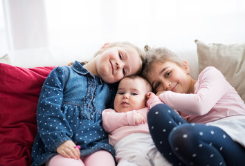 A portrait of three small girls sitting indoors on a sofa.