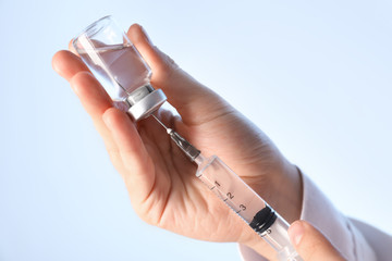 Doctor preparing syringe for injection on light background, closeup