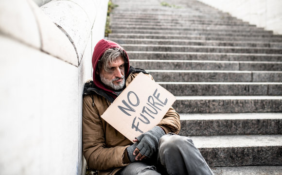 Homeless beggar man sitting outdoors in city holding no future cardboard sign.