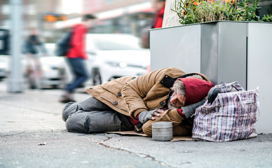 Homeless beggar man lying on the ground outdoors in city asking for money donation.