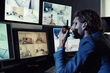 Security guard monitoring modern CCTV cameras in surveillance room