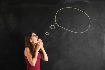 Young woman near blank speech bubble drawn on blackboard