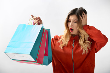 Shocked young woman with shopping bags on white background