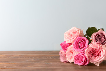 Beautiful bouquet of roses on wooden table against light background
