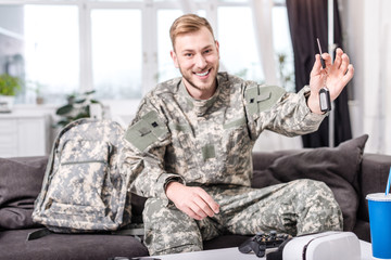 Excited army soldier sitting on couch at home, looking at camera and holding key