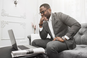 Young African American businessman in a gray suit working behind a laptop.