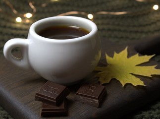 A Cup of espresso with bitter chocolate and autumn leaf on a wooden board