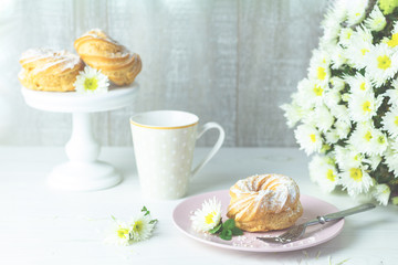 Delicious cake with coconut chips on pink plate on white table, autumn white chrysanthemum and cup of coffee