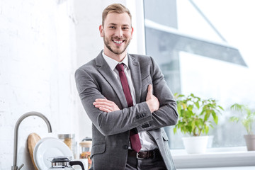 smiling businessman with crossed arms in kitchen looking at camera