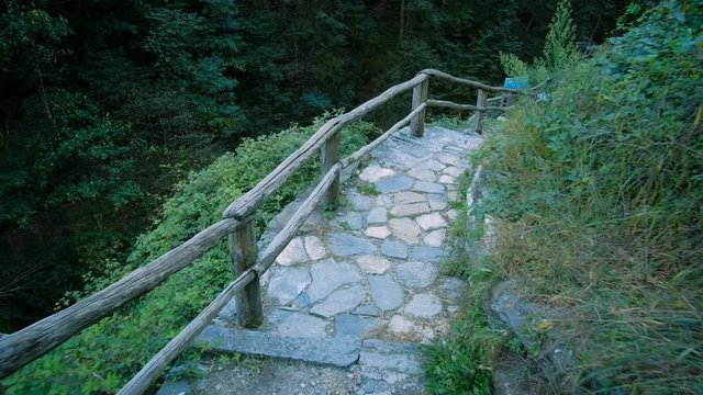 First person view walking along a stone pathway towards an old bridge over a dry river surrounded by forest in the village of Corippo Switzerland. Smooth gliding camera motion in 4K.