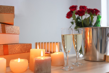 Glasses of champagne with burning candles and gift boxes on wooden table