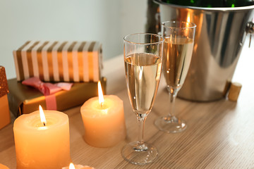 Glasses of champagne with burning candles and gift boxes on wooden table