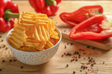 Bowl of tasty potato chips with paprika on wooden background
