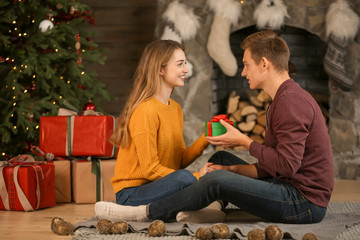 Obraz premium Young woman receiving Christmas gift from her boyfriend at home