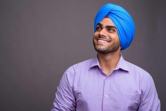 Young handsome Indian businessman wearing turban against gray ba - Powered by Adobe