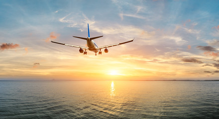 Fototapeta na wymiar Airplane flying over the sea at sunset