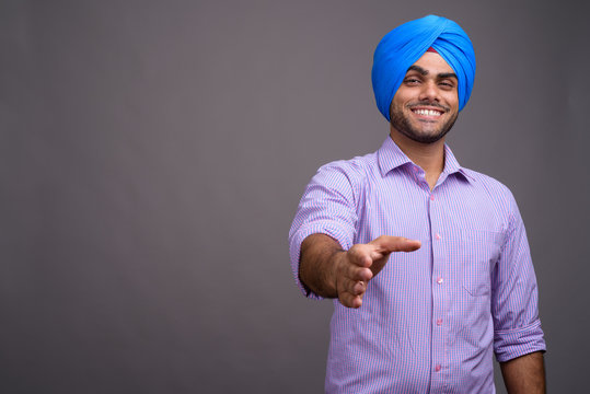 Young handsome Indian businessman wearing turban against gray ba - Powered by Adobe