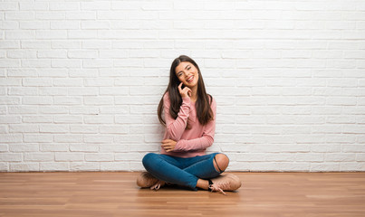 Teenager girl sitting on the floor in a room smiling with a sweet expression