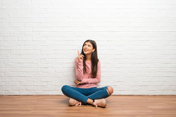 Teenager girl sitting on the floor in a room pointing a great idea and looking up