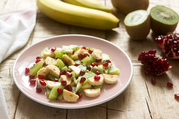 Salad of slices of various fruits and pomegranate seeds on a wooden background.