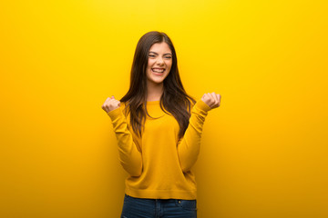 Teenager girl on vibrant yellow background celebrating a victory