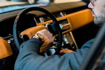 partial view of businessman checking watch in luxury car