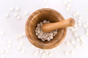 Close-up of small white tablets in a wooden mortar to be ground into powder. Preparation of medicinal mixtures.