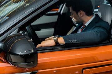 selective focus of stylish businessman sitting in luxury orange car