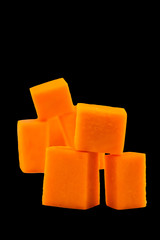 Bright orange cubes. Pieces of sliced pumpkin. Fresh fruit. Vegetarian food. Vertical. Isolated on black background.