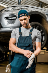 portrait of auto mechanic in uniform wearing protective gloves at auto repair shop