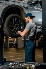 Fototapeta na wymiar auto mechanic in uniform fixing car wheel at auto repair shop