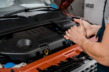 cropped shot of repairman standing at car with opened cowl at auto repair shop