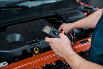 partial view of auto mechanic with multimeter voltmeter checking car battery voltage at mechanic shop
