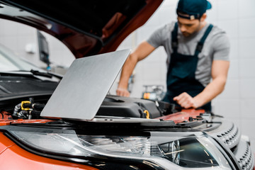 selective focus of laptop and auto mechanic at auto repair shop