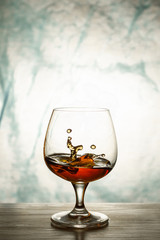 Cognac in a glass goblet on a wooden table with splashes