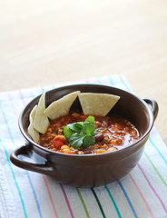 Delicious chili con carne with tortilla in a clay bowl on wooden table
