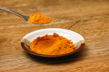 Metal spoon with turmeric spice on wooden table. Macro photography in rustic ambient.
