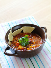 Delicious chili con carne with tortilla in a clay bowl on wooden table