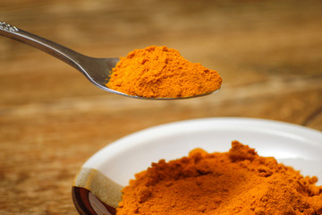 Metal spoon with turmeric spice on wooden table. Macro photography in rustic ambient.