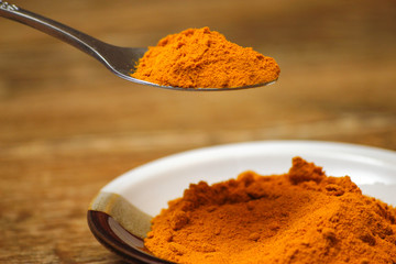 Metal spoon with turmeric spice on wooden table. Macro photography in rustic ambient.