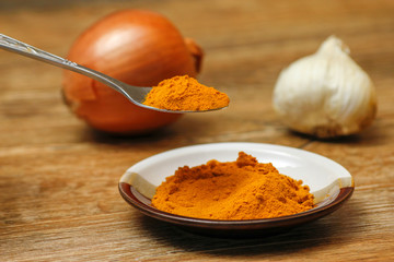 Metal spoon with turmeric spice on wooden table. Macro photography in rustic ambient.