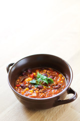 Delicious chili con carne in a clay bowl on wooden table