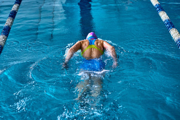 Female athlete swims with a butterfly style. Splashes of water scatter in different directions.