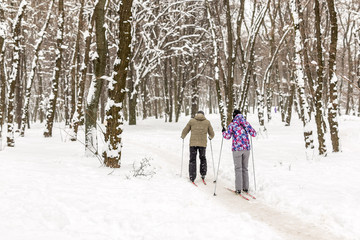 Fototapeta na wymiar Couple of people enjoying cross-country skiing in city park or forest in winter. Family Sport outdoor activities in winter season concept. Healthy lifestyle