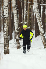 An athlete in sports clothes runs in a snow-covered forest.