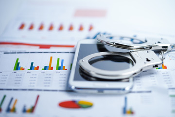Fototapeta premium Metal handcuffs and mobile phone on chart graph background. Hacker economy finance banking static concept.
