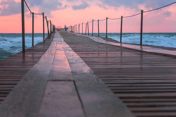Obraz premium Beautiful seascape with pink sunset, pier and storm waves in evening.