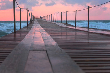 Beautiful seascape with pink sunset, pier and storm waves in evening.