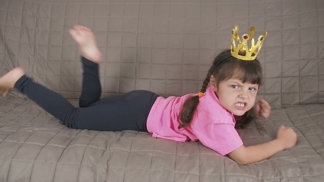 The child manipulates the parents. Aggressive little girl with a crown on her head beats with her feet and hands. Parent manipulation concept.